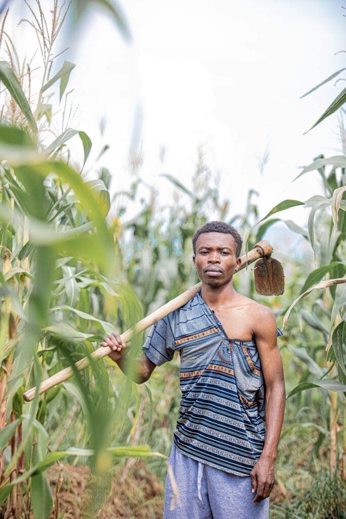 A farmer standing in a corn field in Burundi, holding a hoe on his shoulder.