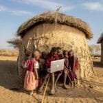Group of African children in a Tanzanian village using a laptop outdoors, engaged in learning.